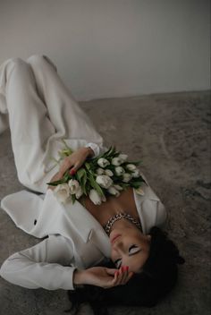 a woman laying on the ground with flowers in her hair and wearing a white suit