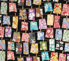 many small square pieces of fabric hanging from clothes pins on a line with flowers and leaves