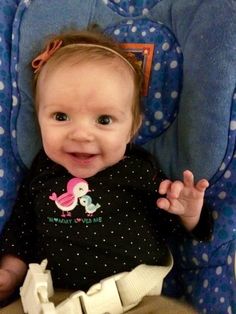 a baby sitting in a blue highchair with her hands up and smiling at the camera