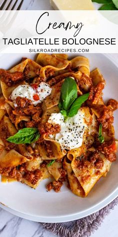 a white plate topped with pasta covered in sauce and cheese, on top of a marble table