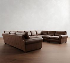 a brown leather couch sitting on top of a hard wood floor next to a white wall