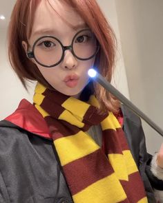 a girl with glasses and a harry potter scarf is holding a wand in her hand