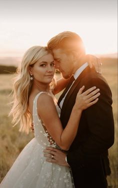 a bride and groom embracing in the middle of a field with sun shining on them