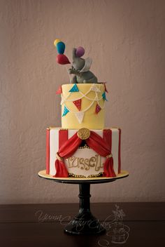 a three tiered cake with an elephant on top and circus decorations around the edges