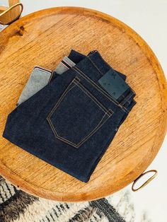 three folded jeans sitting on top of a wooden table next to a pair of glasses