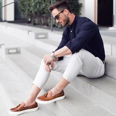 a man sitting on the steps with his feet up and wearing white pants, blue shirt and brown shoes