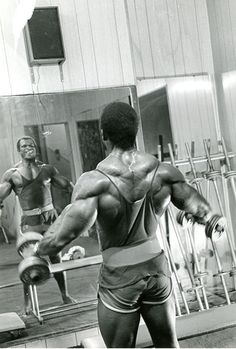 a black and white photo of a man doing exercises in front of a mirror with his back to the camera