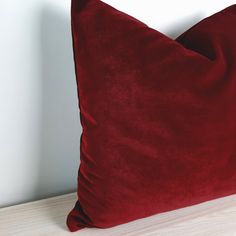 a red velvet pillow sitting on top of a wooden table next to a white wall