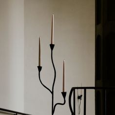 three candles are lit on the top of a black candle holder in front of a white wall