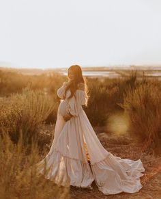 a woman in a long white dress walking through the desert with her back to the camera