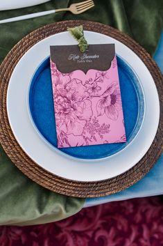 a place setting with blue and pink plates, napkins and silverware on the table