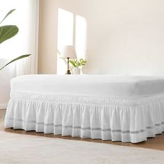 a bed with white ruffled bedspread in a room next to a potted plant