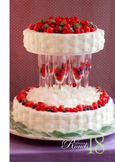 two tiered cake with strawberries and champagne glasses on top, sitting on a purple table cloth