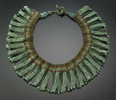 an elaborate necklace with green beads and tassels on a gray background, in the shape of a circle