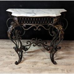 a marble top table with iron scroll work on the legs and bottom, sitting on a hard wood floor