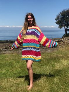 a woman standing in the grass wearing a colorful crochet dress with her arms outstretched