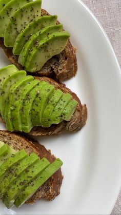 three pieces of bread topped with sliced kiwi on top of a white platter