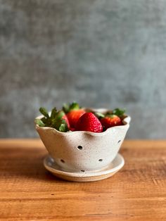 a white bowl filled with strawberries on top of a wooden table next to a gray wall