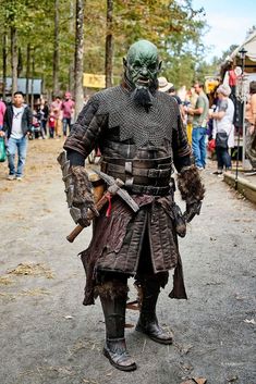 a man dressed up in armor and holding two swords is walking down the street while people look on