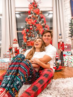 a man and woman sitting on the floor in front of a christmas tree with presents