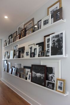 a wall filled with lots of pictures and framed photos next to a wooden floor in front of a white wall