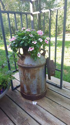 a rusted metal container with pink flowers in it on a wooden deck next to a fence