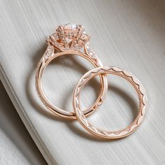 two gold wedding rings sitting on top of a white surface with diamonds in the middle