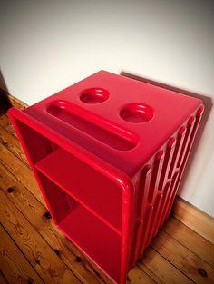 a red plastic object sitting on top of a wooden floor next to a white wall