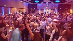 a large group of people dancing in a room with lights on the ceiling and blue lighting