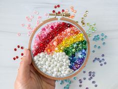 a hand holding a colorful bead and sequins in a wooden embroidery hoop