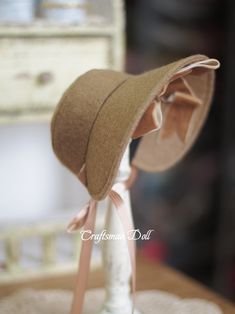 a brown hat is on top of a white vase with a pink ribbon around the brim