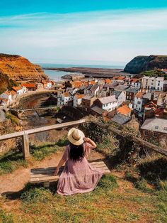 a woman in a hat sitting on a bench looking out at the ocean and buildings