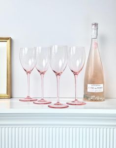 four wine glasses lined up next to a bottle on a mantle with a gold framed mirror