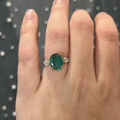 This rare and beautiful green emerald and diamond ring is perfect for any modern engagement! This oval cut emerald marquise diamond ring is finished in 14 karat yellow gold. Sleek modern in design. The center emerald reflects a rich sea green hue. Two (2) sparkling accent diamonds flank the center gemstone. Full of sparkle vibrant color. Finished on a classic 14 karat yellow gold band with a geometric gallery rail. Colored gemstone engagement rings add a personal touch to your special ceremony. Green Oval Ring, Wedding Ring With Emerald Accents, Oval Cut Emerald Engagement Ring, Emerald Oval Ring, Emerald Oval Engagement Ring, Oval Emerald Ring Design, Emerald Ring Designs, Emerald Stone Engagement Ring, Emerald Green Engagement Ring