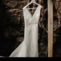 a white wedding dress hanging on a wooden hanger in front of a rock wall