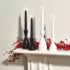 three black and white candles are sitting on a mantle with red berries in the foreground