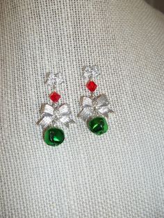 "Bells and Bows Drop Dangle Earrings Christmas Holiday Secret Santa Hostess Gift Simple yet striking design Lovely silver bows are incorporated into this chandelier style earring Smaller bow is the base for these post/stud earrings Embellished with a red crystal then a larger matching bow holds a real jingle bell Bows are aluminum Crystal is glass Bell is colored aluminum Earring length measures 1 3/8\" Earring width measures 5/8\" (widest point is larger bow) Comes in a festive gift box for instant gift giving" Christmas Bazar, Holiday Jewelry Ideas, Green Chandelier, Green Chandeliers, Aluminum Earrings, Earrings Christmas, Silver Bow, Chandelier Style, Homemade Jewelry