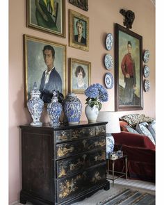 a living room with paintings on the wall and vases sitting on top of a dresser