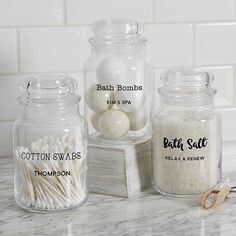 three glass jars filled with cotton swabs on top of a marble countertop