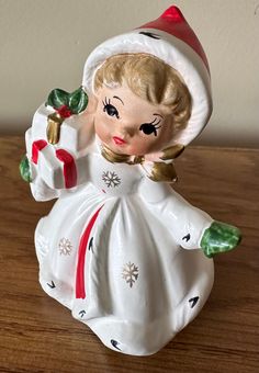 a ceramic figurine that is sitting on a wooden table with a white dress and red hat