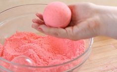 a hand holding a pink ball over a bowl filled with powdered sugar on top of a wooden table