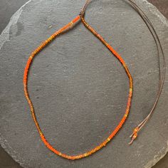 an orange beaded necklace is displayed on a gray stone slab with a hook clasp