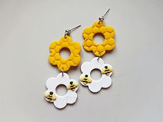 two pairs of yellow and white earrings with flowers on the bottom, one is shaped like a bee