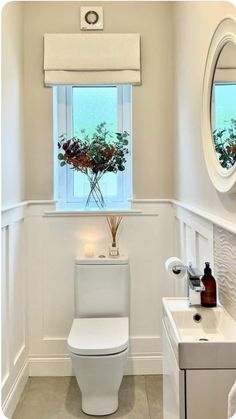 a white toilet sitting next to a sink in a bathroom under a window with a flower vase on it