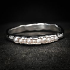 a silver ring with pearls in it on top of a black stone surface and dark background