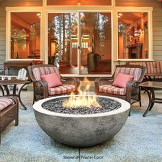 an outdoor fire pit sitting on top of a patio next to chairs and tables in front of a building