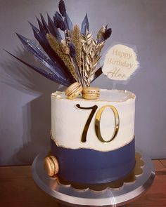 a 70th birthday cake decorated with blue and white frosting, gold decorations and feathers