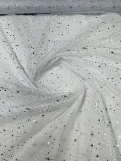 white fabric with silver stars and sparkles in the center, on top of a bed