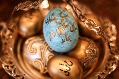 some gold and blue eggs with arabic writing on them sitting in a metal bowl together