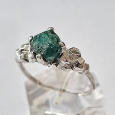 a close up of a ring with a green stone in it on a clear surface